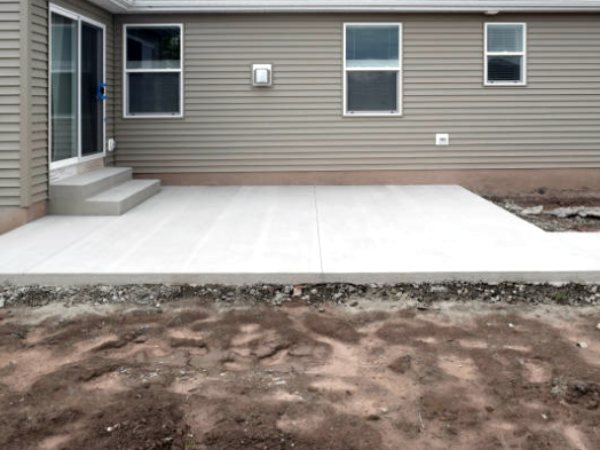 New concrete patio and poured steps behind a house with gray siding