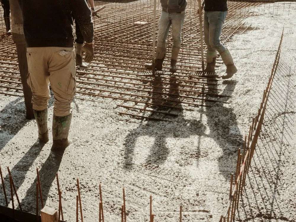 Workers walking on a tied rebar grid while concrete is placed